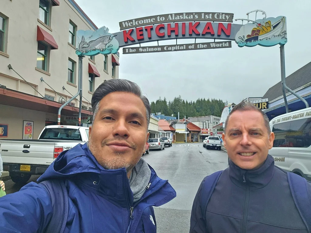 Cruising with Danny and Peter, Holland America Line, Westerdam, Ketchikan, Alaska, United States, Adventure History Thrills | A vibrant collage capturing the Ketchikan Adventure Tour in Alaska, featuring a dynamic log-rolling contest at the Great Alaskan Lumberjack Show with lumberjacks in plaid shirts balancing on a floating log, a rugged UTV navigating a muddy trail through the Tongass National Forest with George Inlet Fjords’ turquoise waters in view, a serene scenic cruise along the Inside Passage with a bald eagle soaring above mist-covered mountains, and a cozy scene at George Inlet Lodge with a rustic table set with craft beers, creamy crab chowder, hot Dungeness crab, and blueberry cheesecake. In the background, Ketchikan’s historic Creek Street showcases colorful buildings on stilts and a Tlingit totem pole, framed by lush greenery and rugged Alaskan peaks, embodying the city’s thrilling adventures and rich cultural heritage.