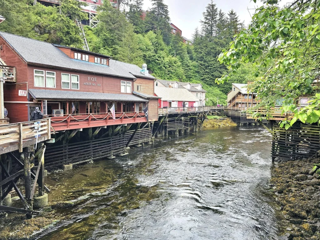 Cruising with Danny and Peter, Holland America Line, Westerdam, Ketchikan, Alaska, United States, Adventure History Thrills | A vibrant collage capturing the Ketchikan Adventure Tour in Alaska, featuring a dynamic log-rolling contest at the Great Alaskan Lumberjack Show with lumberjacks in plaid shirts balancing on a floating log, a rugged UTV navigating a muddy trail through the Tongass National Forest with George Inlet Fjords’ turquoise waters in view, a serene scenic cruise along the Inside Passage with a bald eagle soaring above mist-covered mountains, and a cozy scene at George Inlet Lodge with a rustic table set with craft beers, creamy crab chowder, hot Dungeness crab, and blueberry cheesecake. In the background, Ketchikan’s historic Creek Street showcases colorful buildings on stilts and a Tlingit totem pole, framed by lush greenery and rugged Alaskan peaks, embodying the city’s thrilling adventures and rich cultural heritage.