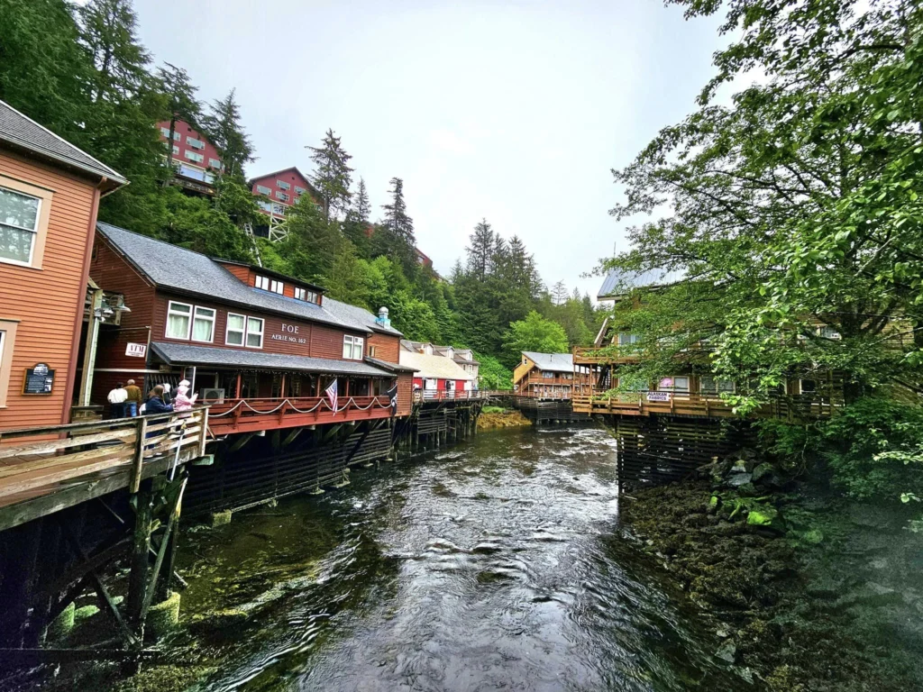 Cruising with Danny and Peter, Holland America Line, Westerdam, Ketchikan, Alaska, United States, Adventure History Thrills | A vibrant collage capturing the Ketchikan Adventure Tour in Alaska, featuring a dynamic log-rolling contest at the Great Alaskan Lumberjack Show with lumberjacks in plaid shirts balancing on a floating log, a rugged UTV navigating a muddy trail through the Tongass National Forest with George Inlet Fjords’ turquoise waters in view, a serene scenic cruise along the Inside Passage with a bald eagle soaring above mist-covered mountains, and a cozy scene at George Inlet Lodge with a rustic table set with craft beers, creamy crab chowder, hot Dungeness crab, and blueberry cheesecake. In the background, Ketchikan’s historic Creek Street showcases colorful buildings on stilts and a Tlingit totem pole, framed by lush greenery and rugged Alaskan peaks, embodying the city’s thrilling adventures and rich cultural heritage.