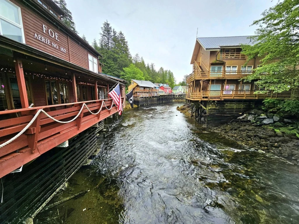 Cruising with Danny and Peter, Holland America Line, Westerdam, Ketchikan, Alaska, United States, Adventure History Thrills | A vibrant collage capturing the Ketchikan Adventure Tour in Alaska, featuring a dynamic log-rolling contest at the Great Alaskan Lumberjack Show with lumberjacks in plaid shirts balancing on a floating log, a rugged UTV navigating a muddy trail through the Tongass National Forest with George Inlet Fjords’ turquoise waters in view, a serene scenic cruise along the Inside Passage with a bald eagle soaring above mist-covered mountains, and a cozy scene at George Inlet Lodge with a rustic table set with craft beers, creamy crab chowder, hot Dungeness crab, and blueberry cheesecake. In the background, Ketchikan’s historic Creek Street showcases colorful buildings on stilts and a Tlingit totem pole, framed by lush greenery and rugged Alaskan peaks, embodying the city’s thrilling adventures and rich cultural heritage.