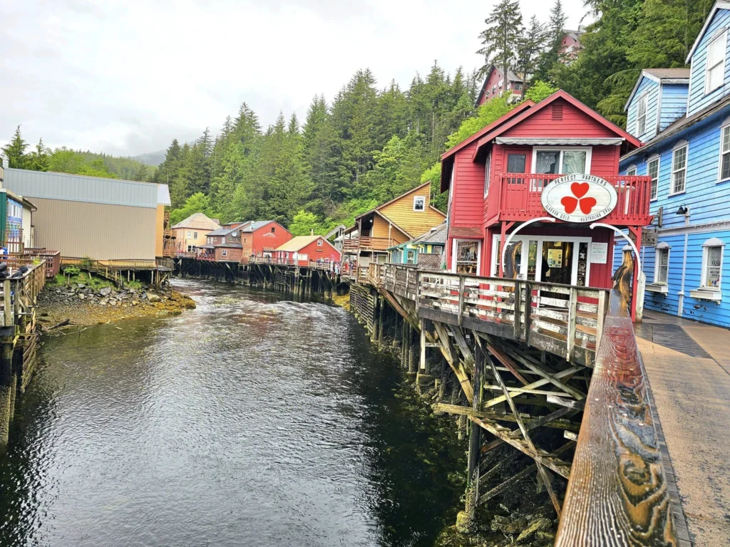 Cruising with Danny and Peter, Holland America Line, Westerdam, Ketchikan, Alaska, United States, Adventure History Thrills | A vibrant collage capturing the Ketchikan Adventure Tour in Alaska, featuring a dynamic log-rolling contest at the Great Alaskan Lumberjack Show with lumberjacks in plaid shirts balancing on a floating log, a rugged UTV navigating a muddy trail through the Tongass National Forest with George Inlet Fjords’ turquoise waters in view, a serene scenic cruise along the Inside Passage with a bald eagle soaring above mist-covered mountains, and a cozy scene at George Inlet Lodge with a rustic table set with craft beers, creamy crab chowder, hot Dungeness crab, and blueberry cheesecake. In the background, Ketchikan’s historic Creek Street showcases colorful buildings on stilts and a Tlingit totem pole, framed by lush greenery and rugged Alaskan peaks, embodying the city’s thrilling adventures and rich cultural heritage.