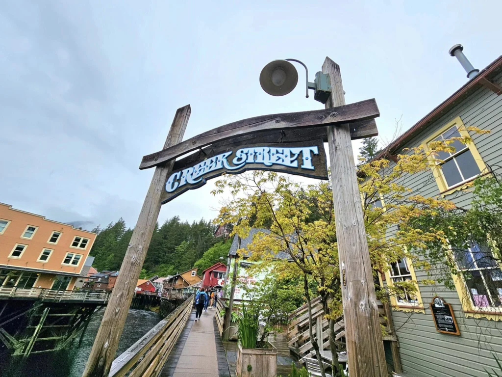 Cruising with Danny and Peter, Holland America Line, Westerdam, Ketchikan, Alaska, United States, Adventure History Thrills | A vibrant collage capturing the Ketchikan Adventure Tour in Alaska, featuring a dynamic log-rolling contest at the Great Alaskan Lumberjack Show with lumberjacks in plaid shirts balancing on a floating log, a rugged UTV navigating a muddy trail through the Tongass National Forest with George Inlet Fjords’ turquoise waters in view, a serene scenic cruise along the Inside Passage with a bald eagle soaring above mist-covered mountains, and a cozy scene at George Inlet Lodge with a rustic table set with craft beers, creamy crab chowder, hot Dungeness crab, and blueberry cheesecake. In the background, Ketchikan’s historic Creek Street showcases colorful buildings on stilts and a Tlingit totem pole, framed by lush greenery and rugged Alaskan peaks, embodying the city’s thrilling adventures and rich cultural heritage.