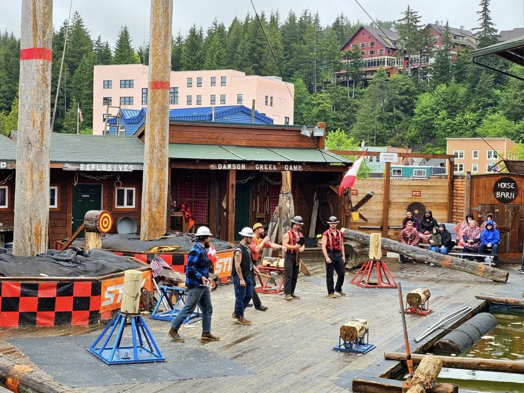 Cruising with Danny and Peter, Holland America Line, Westerdam, Ketchikan, Alaska, United States, Adventure History Thrills | A vibrant collage capturing the Ketchikan Adventure Tour in Alaska, featuring a dynamic log-rolling contest at the Great Alaskan Lumberjack Show with lumberjacks in plaid shirts balancing on a floating log, a rugged UTV navigating a muddy trail through the Tongass National Forest with George Inlet Fjords’ turquoise waters in view, a serene scenic cruise along the Inside Passage with a bald eagle soaring above mist-covered mountains, and a cozy scene at George Inlet Lodge with a rustic table set with craft beers, creamy crab chowder, hot Dungeness crab, and blueberry cheesecake. In the background, Ketchikan’s historic Creek Street showcases colorful buildings on stilts and a Tlingit totem pole, framed by lush greenery and rugged Alaskan peaks, embodying the city’s thrilling adventures and rich cultural heritage.