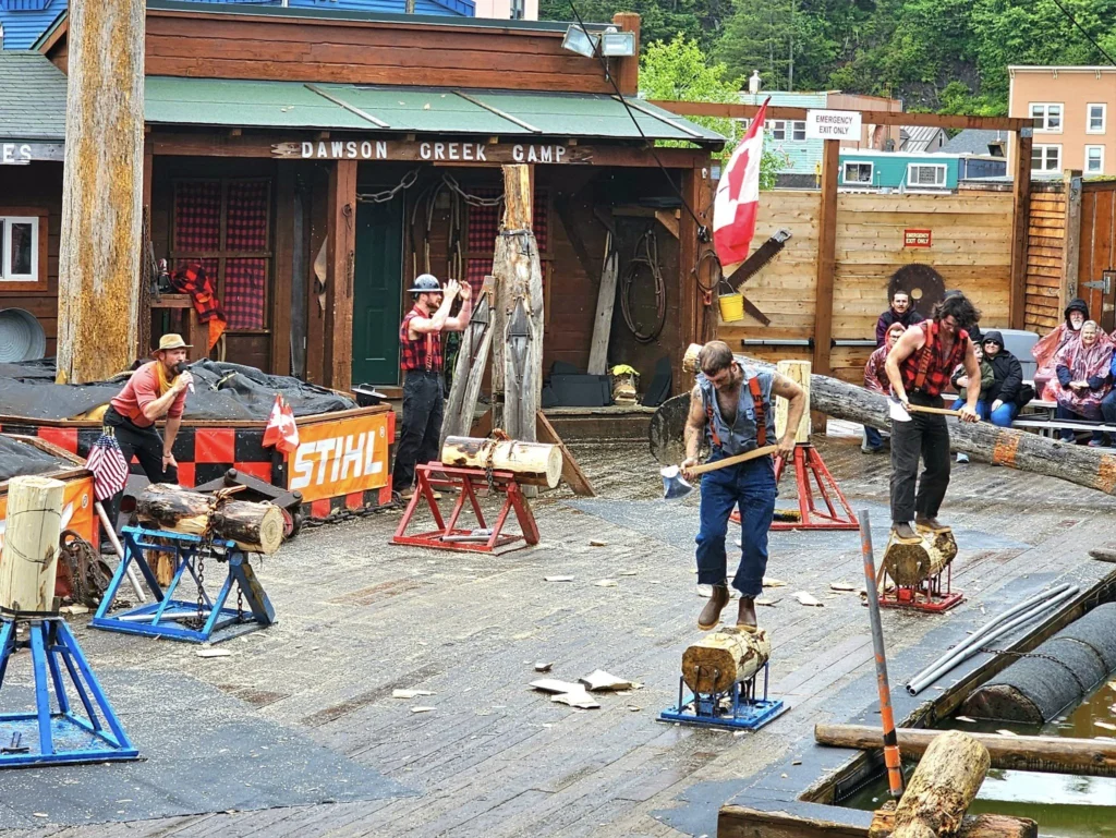 Cruising with Danny and Peter, Holland America Line, Westerdam, Ketchikan, Alaska, United States, Adventure History Thrills | A vibrant collage capturing the Ketchikan Adventure Tour in Alaska, featuring a dynamic log-rolling contest at the Great Alaskan Lumberjack Show with lumberjacks in plaid shirts balancing on a floating log, a rugged UTV navigating a muddy trail through the Tongass National Forest with George Inlet Fjords’ turquoise waters in view, a serene scenic cruise along the Inside Passage with a bald eagle soaring above mist-covered mountains, and a cozy scene at George Inlet Lodge with a rustic table set with craft beers, creamy crab chowder, hot Dungeness crab, and blueberry cheesecake. In the background, Ketchikan’s historic Creek Street showcases colorful buildings on stilts and a Tlingit totem pole, framed by lush greenery and rugged Alaskan peaks, embodying the city’s thrilling adventures and rich cultural heritage.