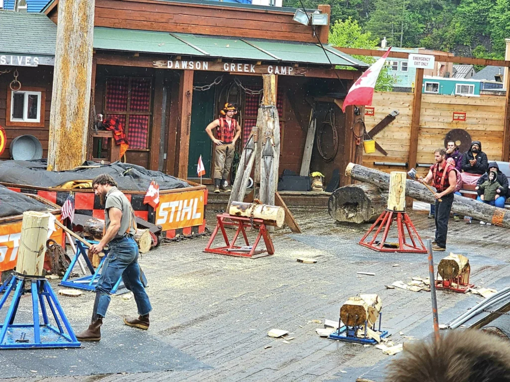 Cruising with Danny and Peter, Holland America Line, Westerdam, Ketchikan, Alaska, United States, Adventure History Thrills | A vibrant collage capturing the Ketchikan Adventure Tour in Alaska, featuring a dynamic log-rolling contest at the Great Alaskan Lumberjack Show with lumberjacks in plaid shirts balancing on a floating log, a rugged UTV navigating a muddy trail through the Tongass National Forest with George Inlet Fjords’ turquoise waters in view, a serene scenic cruise along the Inside Passage with a bald eagle soaring above mist-covered mountains, and a cozy scene at George Inlet Lodge with a rustic table set with craft beers, creamy crab chowder, hot Dungeness crab, and blueberry cheesecake. In the background, Ketchikan’s historic Creek Street showcases colorful buildings on stilts and a Tlingit totem pole, framed by lush greenery and rugged Alaskan peaks, embodying the city’s thrilling adventures and rich cultural heritage.