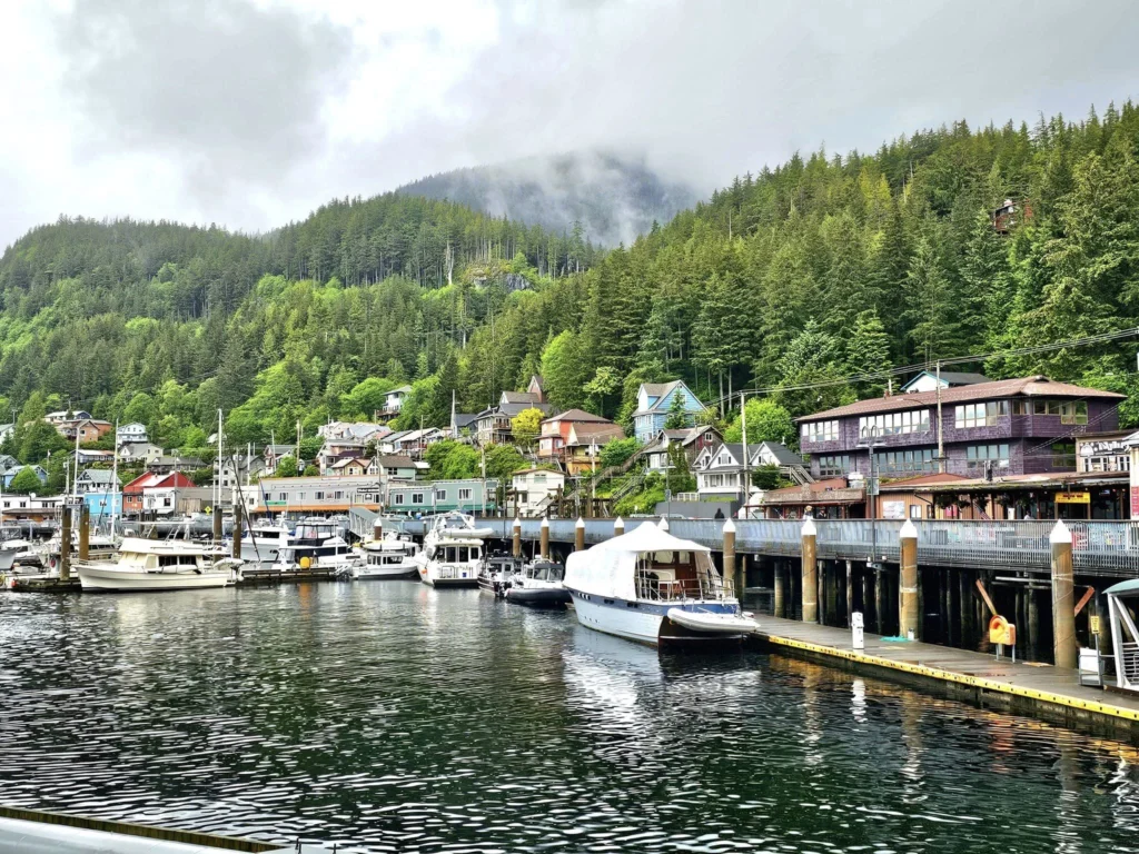 Cruising with Danny and Peter, Holland America Line, Westerdam, Ketchikan, Alaska, United States, Adventure History Thrills | A vibrant collage capturing the Ketchikan Adventure Tour in Alaska, featuring a dynamic log-rolling contest at the Great Alaskan Lumberjack Show with lumberjacks in plaid shirts balancing on a floating log, a rugged UTV navigating a muddy trail through the Tongass National Forest with George Inlet Fjords’ turquoise waters in view, a serene scenic cruise along the Inside Passage with a bald eagle soaring above mist-covered mountains, and a cozy scene at George Inlet Lodge with a rustic table set with craft beers, creamy crab chowder, hot Dungeness crab, and blueberry cheesecake. In the background, Ketchikan’s historic Creek Street showcases colorful buildings on stilts and a Tlingit totem pole, framed by lush greenery and rugged Alaskan peaks, embodying the city’s thrilling adventures and rich cultural heritage.