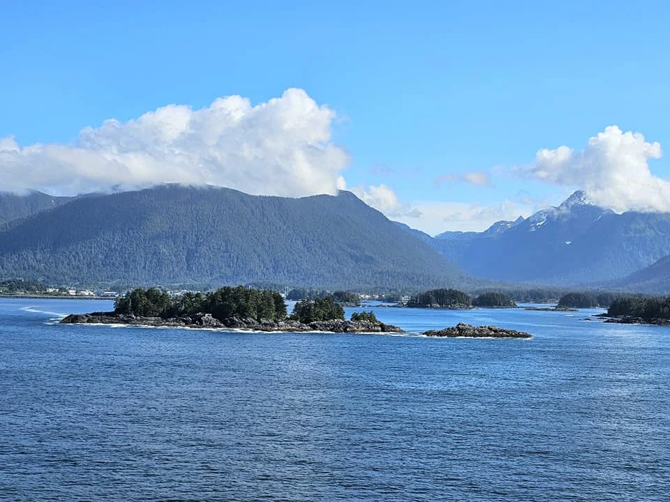 Cruising with Danny and Peter, Holland America Line, Westerdam, Sitka, Alaska, United States | Biking the scenic Sitka Cross Trail through lush Alaskan forests, capturing Sitka's natural beauty and outdoor adventure; a whale breaching in Whale Park, showcasing Sitka Alaska's wildlife; a majestic eagle soaring above, symbolizing the rich wildlife; and an intricate Tlingit totem pole representing the cultural heritage of Sitka, Alaska, all set against the stunning coastal landscape of this Alaskan gem.