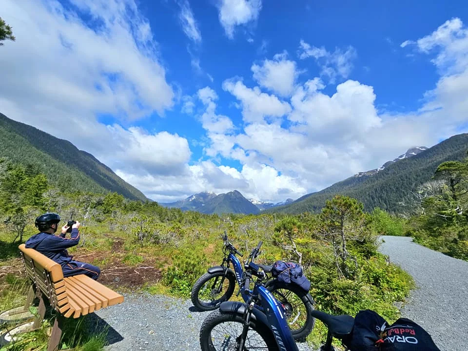 Cruising with Danny and Peter, Holland America Line, Westerdam, Sitka, Alaska, United States | Biking the scenic Sitka Cross Trail through lush Alaskan forests, capturing Sitka's natural beauty and outdoor adventure; a whale breaching in Whale Park, showcasing Sitka Alaska's wildlife; a majestic eagle soaring above, symbolizing the rich wildlife; and an intricate Tlingit totem pole representing the cultural heritage of Sitka, Alaska, all set against the stunning coastal landscape of this Alaskan gem.