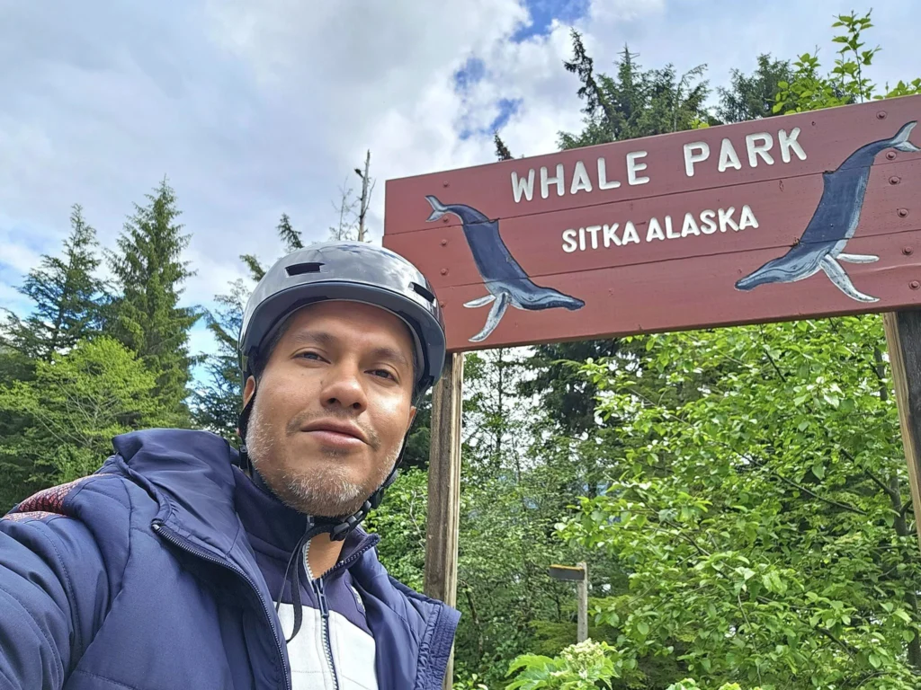 Cruising with Danny and Peter, Holland America Line, Westerdam, Sitka, Alaska, United States | Biking the scenic Sitka Cross Trail through lush Alaskan forests, capturing Sitka's natural beauty and outdoor adventure; a whale breaching in Whale Park, showcasing Sitka Alaska's wildlife; a majestic eagle soaring above, symbolizing the rich wildlife; and an intricate Tlingit totem pole representing the cultural heritage of Sitka, Alaska, all set against the stunning coastal landscape of this Alaskan gem.