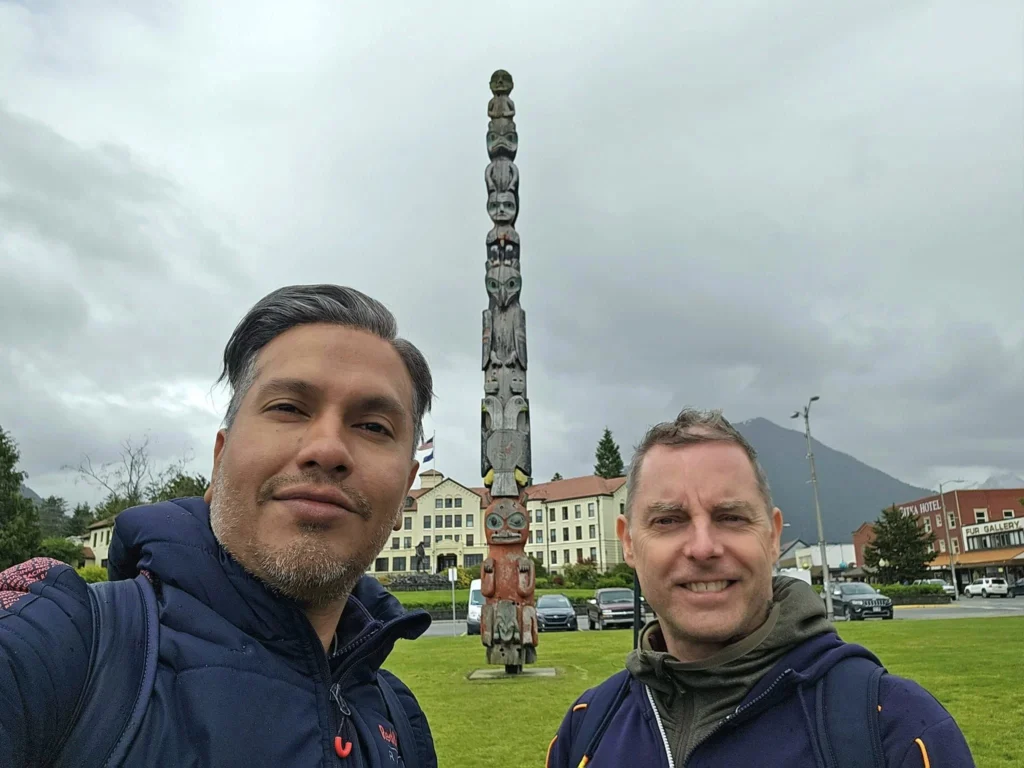 Cruising with Danny and Peter, Holland America Line, Westerdam, Sitka, Alaska, United States | Biking the scenic Sitka Cross Trail through lush Alaskan forests, capturing Sitka's natural beauty and outdoor adventure; a whale breaching in Whale Park, showcasing Sitka Alaska's wildlife; a majestic eagle soaring above, symbolizing the rich wildlife; and an intricate Tlingit totem pole representing the cultural heritage of Sitka, Alaska, all set against the stunning coastal landscape of this Alaskan gem.