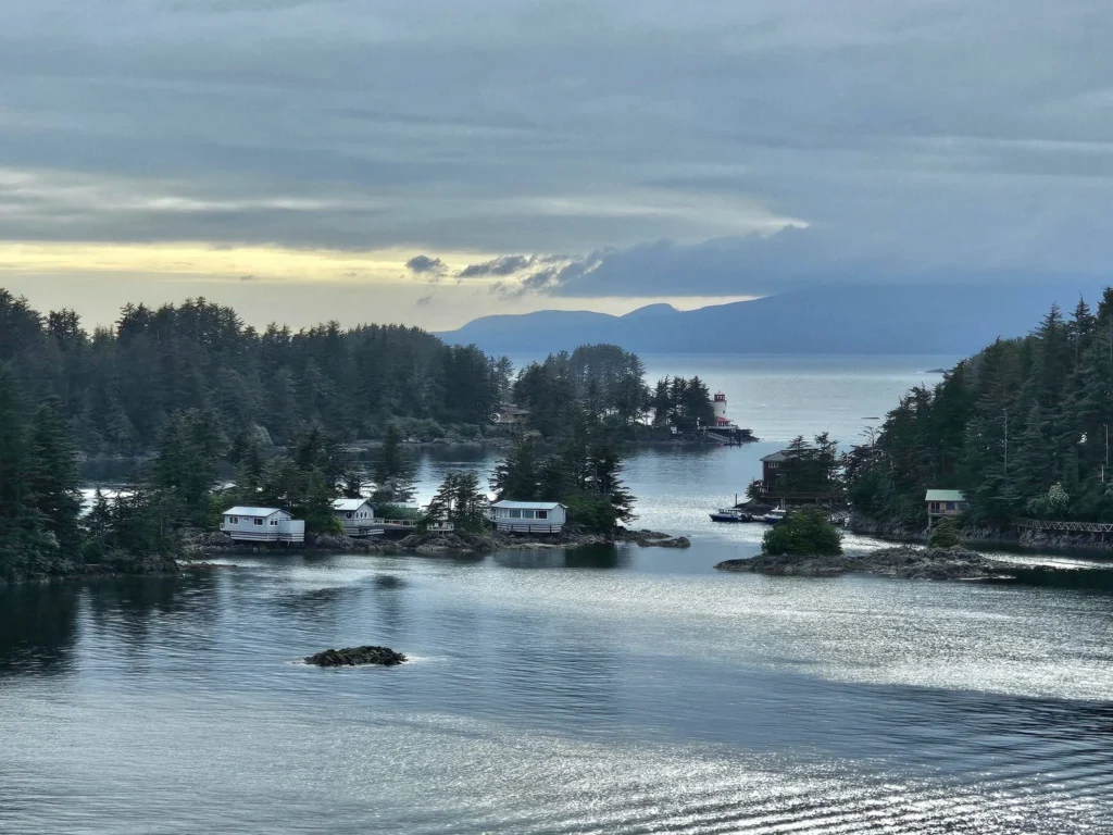 Cruising with Danny and Peter, Holland America Line, Westerdam, Sitka, Alaska, United States | Biking the scenic Sitka Cross Trail through lush Alaskan forests, capturing Sitka's natural beauty and outdoor adventure; a whale breaching in Whale Park, showcasing Sitka Alaska's wildlife; a majestic eagle soaring above, symbolizing the rich wildlife; and an intricate Tlingit totem pole representing the cultural heritage of Sitka, Alaska, all set against the stunning coastal landscape of this Alaskan gem.