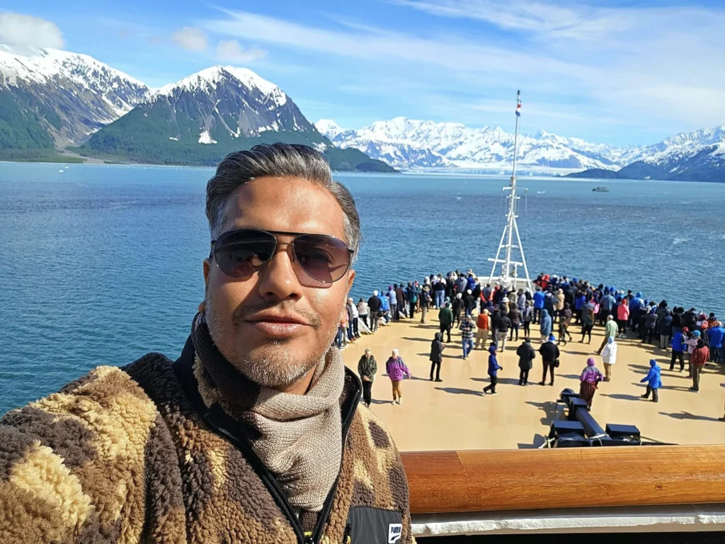 Cruising with Danny and Peter, Holland America Line, Westerdam, Hubbard Glacier, Alaska, United States | View of Hubbard Glacier from the boat during an unforgettable tour, showcasing stunning blue ice and calm Arctic waters. Thrilling ice calving event captures large chunks of ice breaking off and crashing into the water. Mirror-like reflection of the glacier on still waters highlights its majestic blue hues. A delightful picnic with the glacier in the background combines delicious food with breathtaking views, while a close-up of the glacier's intricate ice formations shows deep crevasses and jagged edges.