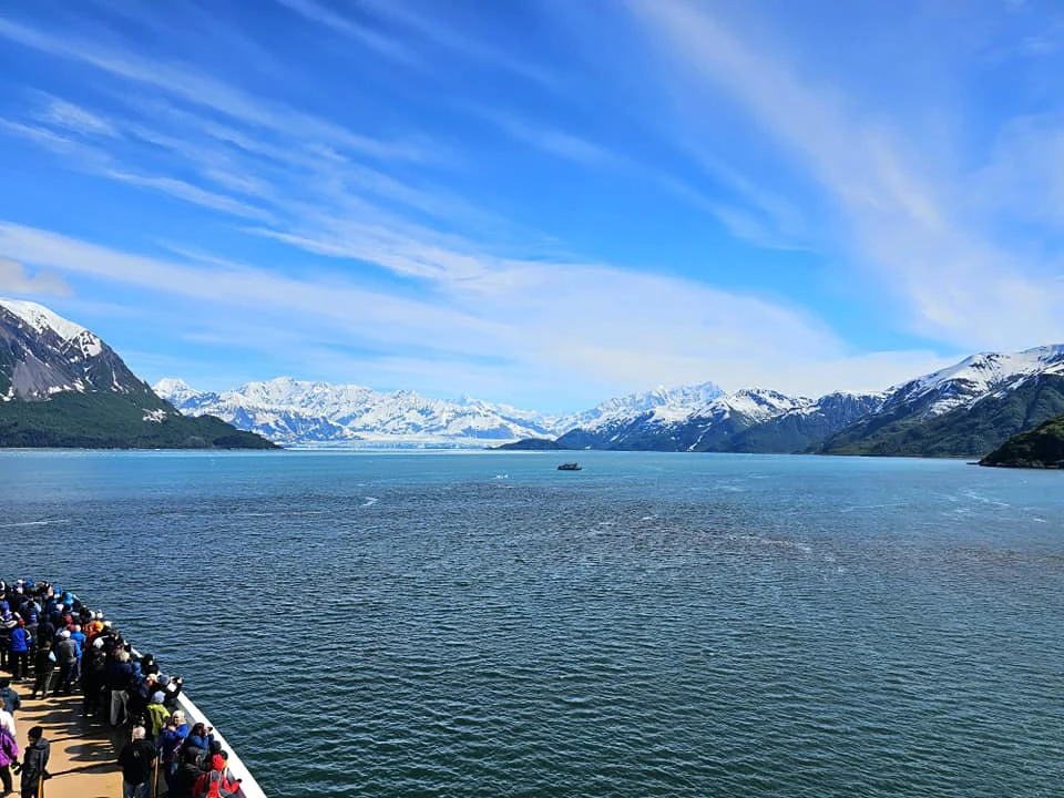 Cruising with Danny and Peter, Holland America Line, Westerdam, Hubbard Glacier, Alaska, United States | View of Hubbard Glacier from the boat during an unforgettable tour, showcasing stunning blue ice and calm Arctic waters. Thrilling ice calving event captures large chunks of ice breaking off and crashing into the water. Mirror-like reflection of the glacier on still waters highlights its majestic blue hues. A delightful picnic with the glacier in the background combines delicious food with breathtaking views, while a close-up of the glacier's intricate ice formations shows deep crevasses and jagged edges.
