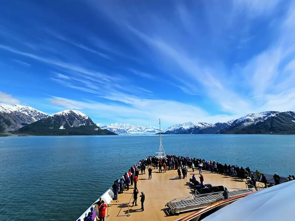 Cruising with Danny and Peter, Holland America Line, Westerdam, Hubbard Glacier, Alaska, United States | View of Hubbard Glacier from the boat during an unforgettable tour, showcasing stunning blue ice and calm Arctic waters. Thrilling ice calving event captures large chunks of ice breaking off and crashing into the water. Mirror-like reflection of the glacier on still waters highlights its majestic blue hues. A delightful picnic with the glacier in the background combines delicious food with breathtaking views, while a close-up of the glacier's intricate ice formations shows deep crevasses and jagged edges.