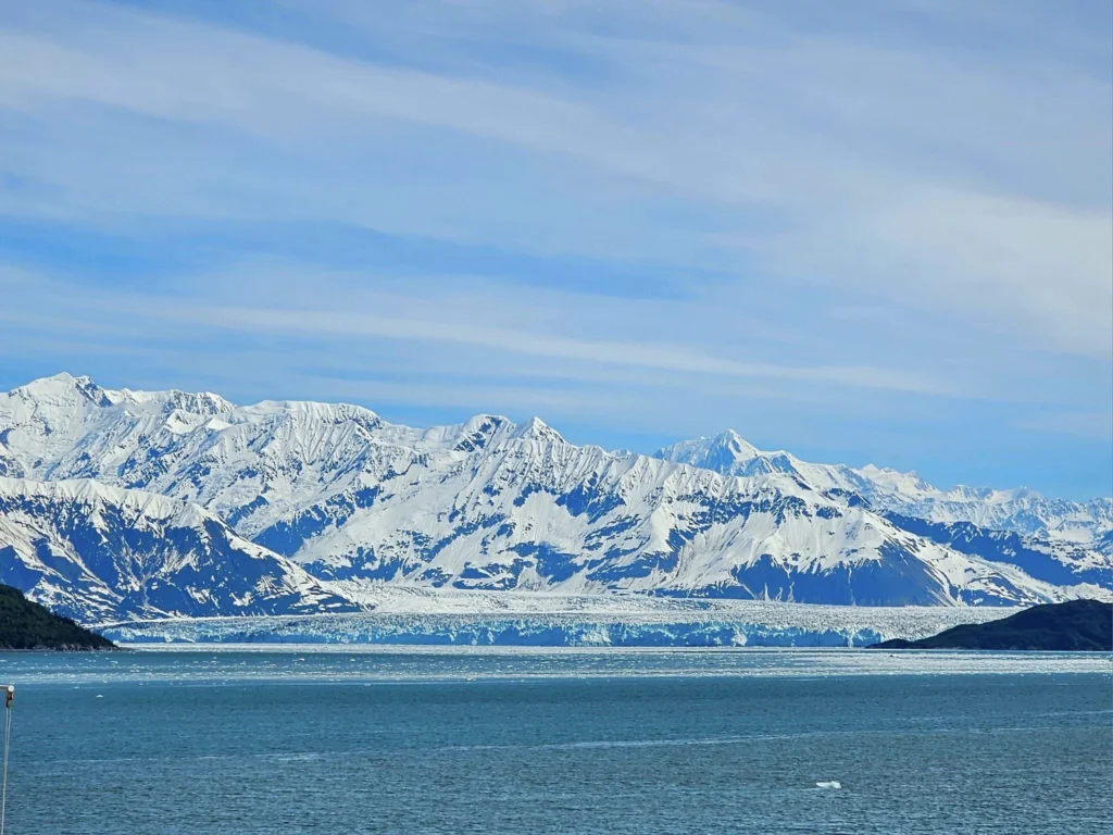 Cruising with Danny and Peter, Holland America Line, Westerdam, Hubbard Glacier, Alaska, United States | View of Hubbard Glacier from the boat during an unforgettable tour, showcasing stunning blue ice and calm Arctic waters. Thrilling ice calving event captures large chunks of ice breaking off and crashing into the water. Mirror-like reflection of the glacier on still waters highlights its majestic blue hues. A delightful picnic with the glacier in the background combines delicious food with breathtaking views, while a close-up of the glacier's intricate ice formations shows deep crevasses and jagged edges.