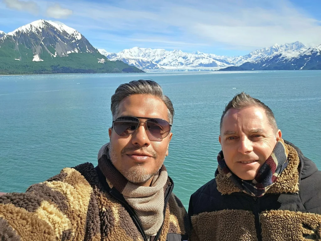 Cruising with Danny and Peter, Holland America Line, Westerdam, Hubbard Glacier, Alaska, United States | View of Hubbard Glacier from the boat during an unforgettable tour, showcasing stunning blue ice and calm Arctic waters. Thrilling ice calving event captures large chunks of ice breaking off and crashing into the water. Mirror-like reflection of the glacier on still waters highlights its majestic blue hues. A delightful picnic with the glacier in the background combines delicious food with breathtaking views, while a close-up of the glacier's intricate ice formations shows deep crevasses and jagged edges.