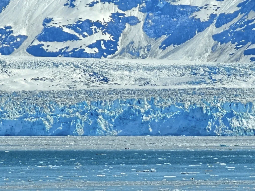 Cruising with Danny and Peter, Holland America Line, Westerdam, Hubbard Glacier, Alaska, United States | View of Hubbard Glacier from the boat during an unforgettable tour, showcasing stunning blue ice and calm Arctic waters. Thrilling ice calving event captures large chunks of ice breaking off and crashing into the water. Mirror-like reflection of the glacier on still waters highlights its majestic blue hues. A delightful picnic with the glacier in the background combines delicious food with breathtaking views, while a close-up of the glacier's intricate ice formations shows deep crevasses and jagged edges.