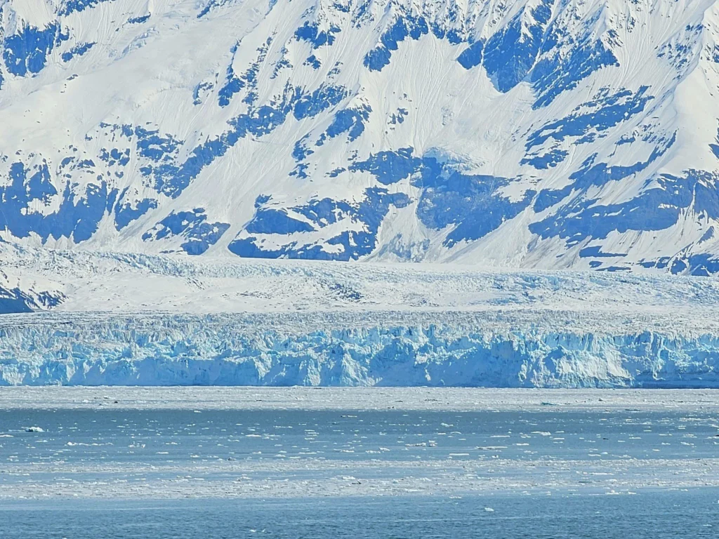 Cruising with Danny and Peter, Holland America Line, Westerdam, Hubbard Glacier, Alaska, United States | View of Hubbard Glacier from the boat during an unforgettable tour, showcasing stunning blue ice and calm Arctic waters. Thrilling ice calving event captures large chunks of ice breaking off and crashing into the water. Mirror-like reflection of the glacier on still waters highlights its majestic blue hues. A delightful picnic with the glacier in the background combines delicious food with breathtaking views, while a close-up of the glacier's intricate ice formations shows deep crevasses and jagged edges.