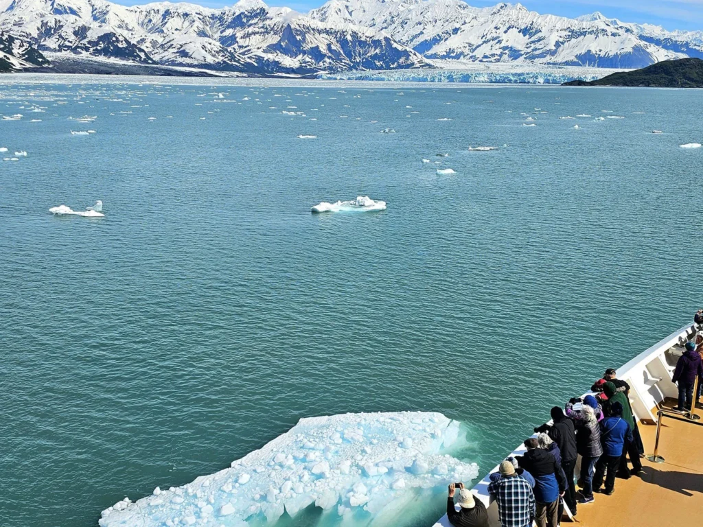 Cruising with Danny and Peter, Holland America Line, Westerdam, Hubbard Glacier, Alaska, United States | View of Hubbard Glacier from the boat during an unforgettable tour, showcasing stunning blue ice and calm Arctic waters. Thrilling ice calving event captures large chunks of ice breaking off and crashing into the water. Mirror-like reflection of the glacier on still waters highlights its majestic blue hues. A delightful picnic with the glacier in the background combines delicious food with breathtaking views, while a close-up of the glacier's intricate ice formations shows deep crevasses and jagged edges.