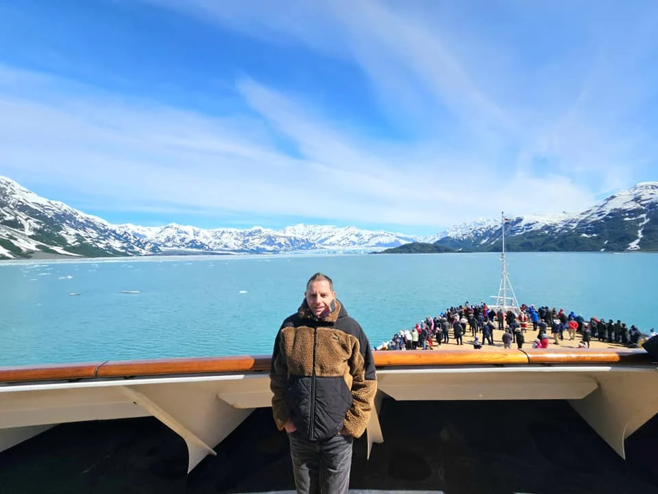 Cruising with Danny and Peter, Holland America Line, Westerdam, Hubbard Glacier, Alaska, United States | View of Hubbard Glacier from the boat during an unforgettable tour, showcasing stunning blue ice and calm Arctic waters. Thrilling ice calving event captures large chunks of ice breaking off and crashing into the water. Mirror-like reflection of the glacier on still waters highlights its majestic blue hues. A delightful picnic with the glacier in the background combines delicious food with breathtaking views, while a close-up of the glacier's intricate ice formations shows deep crevasses and jagged edges.