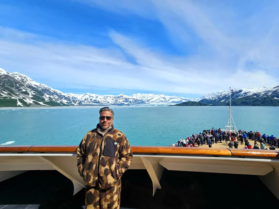 Cruising with Danny and Peter, Holland America Line, Westerdam, Hubbard Glacier, Alaska, United States | View of Hubbard Glacier from the boat during an unforgettable tour, showcasing stunning blue ice and calm Arctic waters. Thrilling ice calving event captures large chunks of ice breaking off and crashing into the water. Mirror-like reflection of the glacier on still waters highlights its majestic blue hues. A delightful picnic with the glacier in the background combines delicious food with breathtaking views, while a close-up of the glacier's intricate ice formations shows deep crevasses and jagged edges.