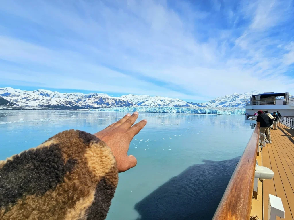 Cruising with Danny and Peter, Holland America Line, Westerdam, Hubbard Glacier, Alaska, United States | View of Hubbard Glacier from the boat during an unforgettable tour, showcasing stunning blue ice and calm Arctic waters. Thrilling ice calving event captures large chunks of ice breaking off and crashing into the water. Mirror-like reflection of the glacier on still waters highlights its majestic blue hues. A delightful picnic with the glacier in the background combines delicious food with breathtaking views, while a close-up of the glacier's intricate ice formations shows deep crevasses and jagged edges.
