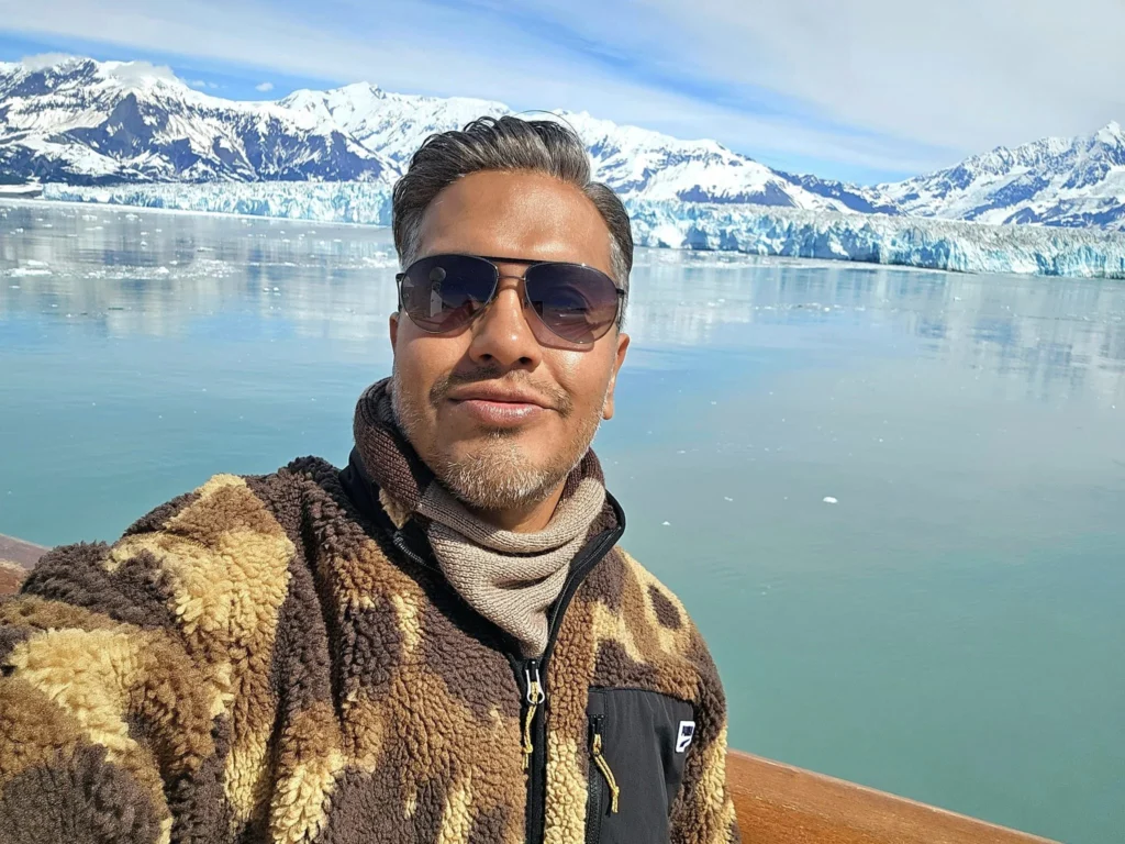 Cruising with Danny and Peter, Holland America Line, Westerdam, Hubbard Glacier, Alaska, United States | View of Hubbard Glacier from the boat during an unforgettable tour, showcasing stunning blue ice and calm Arctic waters. Thrilling ice calving event captures large chunks of ice breaking off and crashing into the water. Mirror-like reflection of the glacier on still waters highlights its majestic blue hues. A delightful picnic with the glacier in the background combines delicious food with breathtaking views, while a close-up of the glacier's intricate ice formations shows deep crevasses and jagged edges.