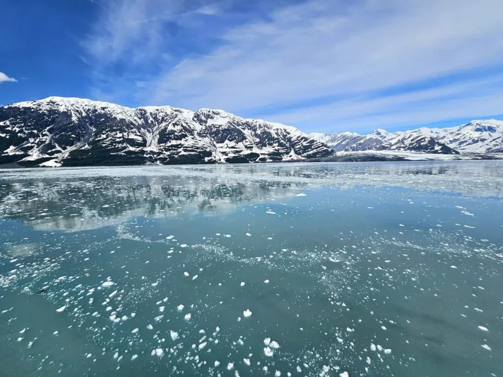 Cruising with Danny and Peter, Holland America Line, Westerdam, Hubbard Glacier, Alaska, United States | View of Hubbard Glacier from the boat during an unforgettable tour, showcasing stunning blue ice and calm Arctic waters. Thrilling ice calving event captures large chunks of ice breaking off and crashing into the water. Mirror-like reflection of the glacier on still waters highlights its majestic blue hues. A delightful picnic with the glacier in the background combines delicious food with breathtaking views, while a close-up of the glacier's intricate ice formations shows deep crevasses and jagged edges.