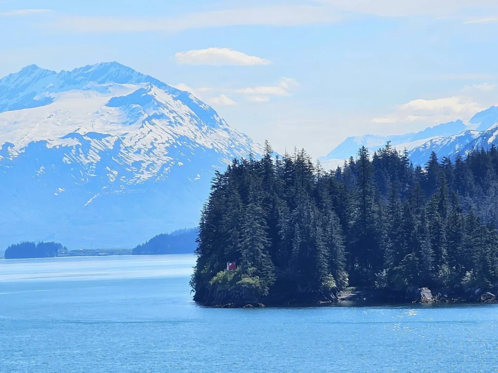 Cruising with Danny and Peter, Holland America Line, Westerdam, Prince William Sound, Valdez, Alaska, United States | A serene panorama of Prince William Sound at dawn, with the luxurious Westerdam cruise ship gliding through calm waters, surrounded by snow-capped mountains and glowing glaciers under a soft pink sky. Humpback whales breach the surface, their tails splashing against the reflective water, while sea otters float playfully in kelp beds and a bald eagle soars overhead. In Valdez Glacier Lake, vibrant blue icebergs drift peacefully, with kayakers in colorful kayaks paddling through the icy maze, dwarfed by the towering Valdez Glacier’s rugged ice face in the background. The Westerdam’s elegant deck features passengers enjoying a gourmet breakfast with panoramic views of the Alaskan wilderness, capturing the harmonious blend of luxury and nature.