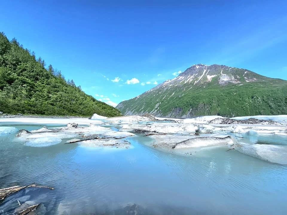 Cruising with Danny and Peter, Holland America Line, Westerdam, Prince William Sound, Valdez, Alaska, United States | A serene panorama of Prince William Sound at dawn, with the luxurious Westerdam cruise ship gliding through calm waters, surrounded by snow-capped mountains and glowing glaciers under a soft pink sky. Humpback whales breach the surface, their tails splashing against the reflective water, while sea otters float playfully in kelp beds and a bald eagle soars overhead. In Valdez Glacier Lake, vibrant blue icebergs drift peacefully, with kayakers in colorful kayaks paddling through the icy maze, dwarfed by the towering Valdez Glacier’s rugged ice face in the background. The Westerdam’s elegant deck features passengers enjoying a gourmet breakfast with panoramic views of the Alaskan wilderness, capturing the harmonious blend of luxury and nature.