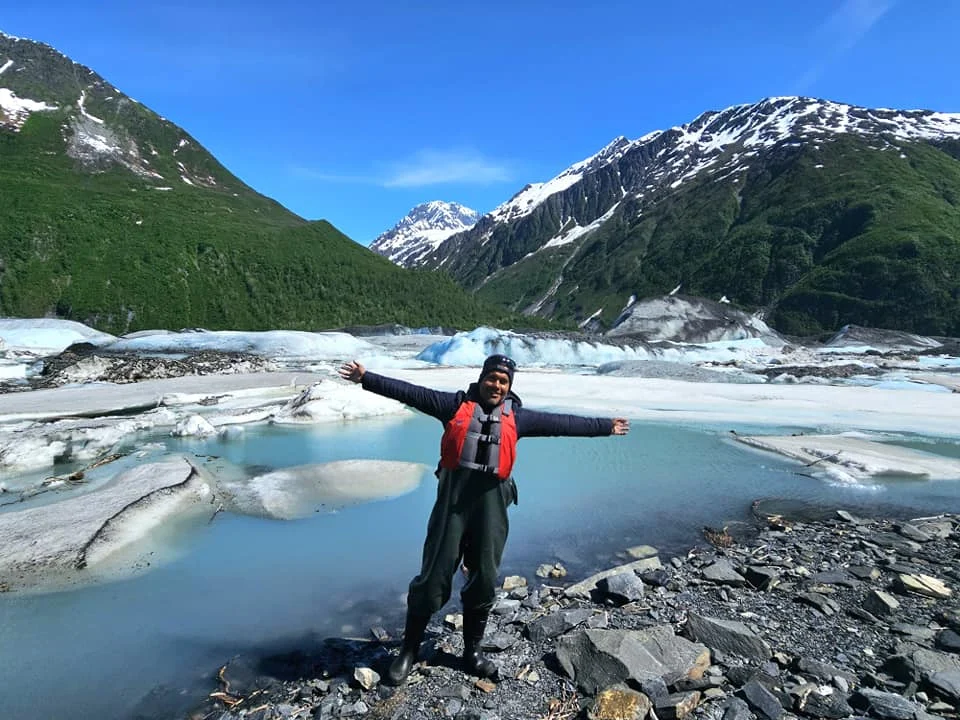 Cruising with Danny and Peter, Holland America Line, Westerdam, Prince William Sound, Valdez, Alaska, United States | A serene panorama of Prince William Sound at dawn, with the luxurious Westerdam cruise ship gliding through calm waters, surrounded by snow-capped mountains and glowing glaciers under a soft pink sky. Humpback whales breach the surface, their tails splashing against the reflective water, while sea otters float playfully in kelp beds and a bald eagle soars overhead. In Valdez Glacier Lake, vibrant blue icebergs drift peacefully, with kayakers in colorful kayaks paddling through the icy maze, dwarfed by the towering Valdez Glacier’s rugged ice face in the background. The Westerdam’s elegant deck features passengers enjoying a gourmet breakfast with panoramic views of the Alaskan wilderness, capturing the harmonious blend of luxury and nature.