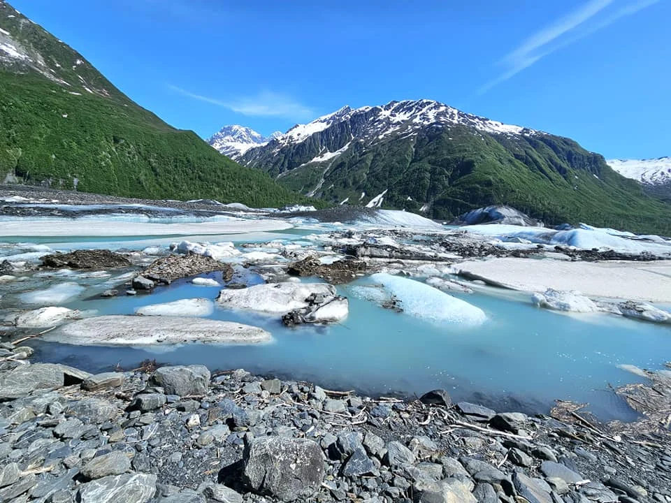 Cruising with Danny and Peter, Holland America Line, Westerdam, Prince William Sound, Valdez, Alaska, United States | A serene panorama of Prince William Sound at dawn, with the luxurious Westerdam cruise ship gliding through calm waters, surrounded by snow-capped mountains and glowing glaciers under a soft pink sky. Humpback whales breach the surface, their tails splashing against the reflective water, while sea otters float playfully in kelp beds and a bald eagle soars overhead. In Valdez Glacier Lake, vibrant blue icebergs drift peacefully, with kayakers in colorful kayaks paddling through the icy maze, dwarfed by the towering Valdez Glacier’s rugged ice face in the background. The Westerdam’s elegant deck features passengers enjoying a gourmet breakfast with panoramic views of the Alaskan wilderness, capturing the harmonious blend of luxury and nature.