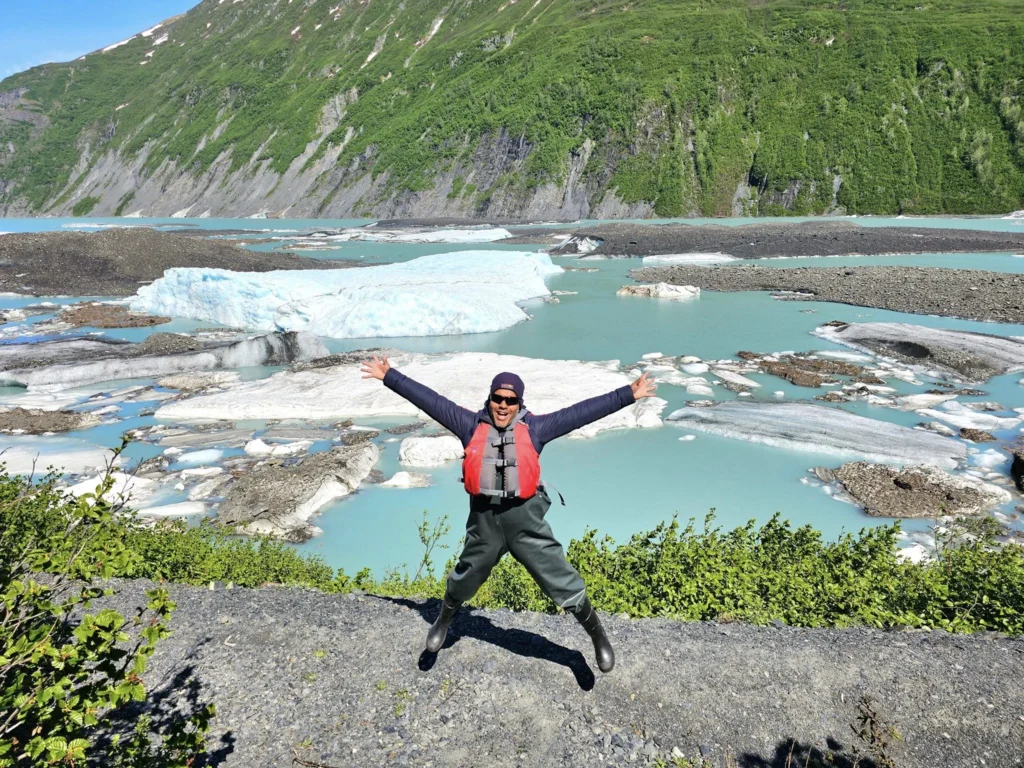 Cruising with Danny and Peter, Holland America Line, Westerdam, Prince William Sound, Valdez, Alaska, United States | A serene panorama of Prince William Sound at dawn, with the luxurious Westerdam cruise ship gliding through calm waters, surrounded by snow-capped mountains and glowing glaciers under a soft pink sky. Humpback whales breach the surface, their tails splashing against the reflective water, while sea otters float playfully in kelp beds and a bald eagle soars overhead. In Valdez Glacier Lake, vibrant blue icebergs drift peacefully, with kayakers in colorful kayaks paddling through the icy maze, dwarfed by the towering Valdez Glacier’s rugged ice face in the background. The Westerdam’s elegant deck features passengers enjoying a gourmet breakfast with panoramic views of the Alaskan wilderness, capturing the harmonious blend of luxury and nature.