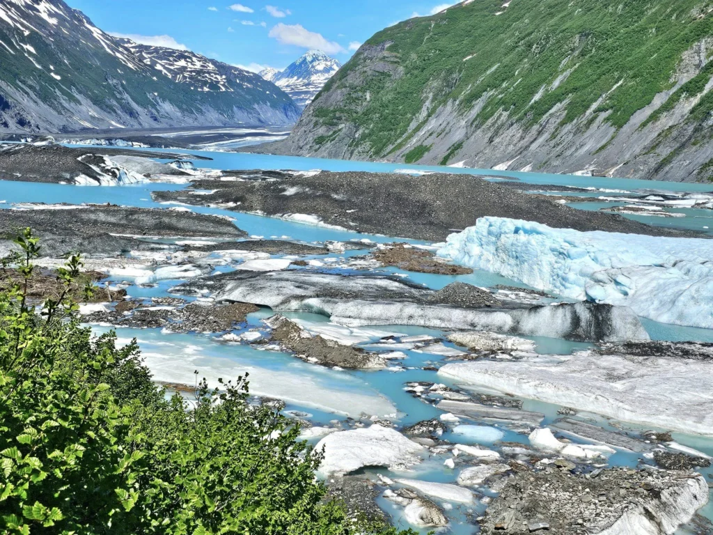 Cruising with Danny and Peter, Holland America Line, Westerdam, Prince William Sound, Valdez, Alaska, United States | A serene panorama of Prince William Sound at dawn, with the luxurious Westerdam cruise ship gliding through calm waters, surrounded by snow-capped mountains and glowing glaciers under a soft pink sky. Humpback whales breach the surface, their tails splashing against the reflective water, while sea otters float playfully in kelp beds and a bald eagle soars overhead. In Valdez Glacier Lake, vibrant blue icebergs drift peacefully, with kayakers in colorful kayaks paddling through the icy maze, dwarfed by the towering Valdez Glacier’s rugged ice face in the background. The Westerdam’s elegant deck features passengers enjoying a gourmet breakfast with panoramic views of the Alaskan wilderness, capturing the harmonious blend of luxury and nature.