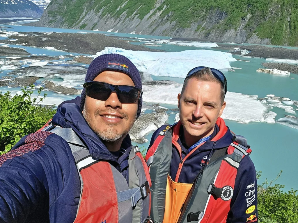 Cruising with Danny and Peter, Holland America Line, Westerdam, Prince William Sound, Valdez, Alaska, United States | A serene panorama of Prince William Sound at dawn, with the luxurious Westerdam cruise ship gliding through calm waters, surrounded by snow-capped mountains and glowing glaciers under a soft pink sky. Humpback whales breach the surface, their tails splashing against the reflective water, while sea otters float playfully in kelp beds and a bald eagle soars overhead. In Valdez Glacier Lake, vibrant blue icebergs drift peacefully, with kayakers in colorful kayaks paddling through the icy maze, dwarfed by the towering Valdez Glacier’s rugged ice face in the background. The Westerdam’s elegant deck features passengers enjoying a gourmet breakfast with panoramic views of the Alaskan wilderness, capturing the harmonious blend of luxury and nature.