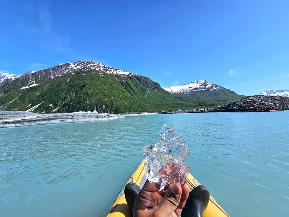 Cruising with Danny and Peter, Holland America Line, Westerdam, Prince William Sound, Valdez, Alaska, United States | A serene panorama of Prince William Sound at dawn, with the luxurious Westerdam cruise ship gliding through calm waters, surrounded by snow-capped mountains and glowing glaciers under a soft pink sky. Humpback whales breach the surface, their tails splashing against the reflective water, while sea otters float playfully in kelp beds and a bald eagle soars overhead. In Valdez Glacier Lake, vibrant blue icebergs drift peacefully, with kayakers in colorful kayaks paddling through the icy maze, dwarfed by the towering Valdez Glacier’s rugged ice face in the background. The Westerdam’s elegant deck features passengers enjoying a gourmet breakfast with panoramic views of the Alaskan wilderness, capturing the harmonious blend of luxury and nature.