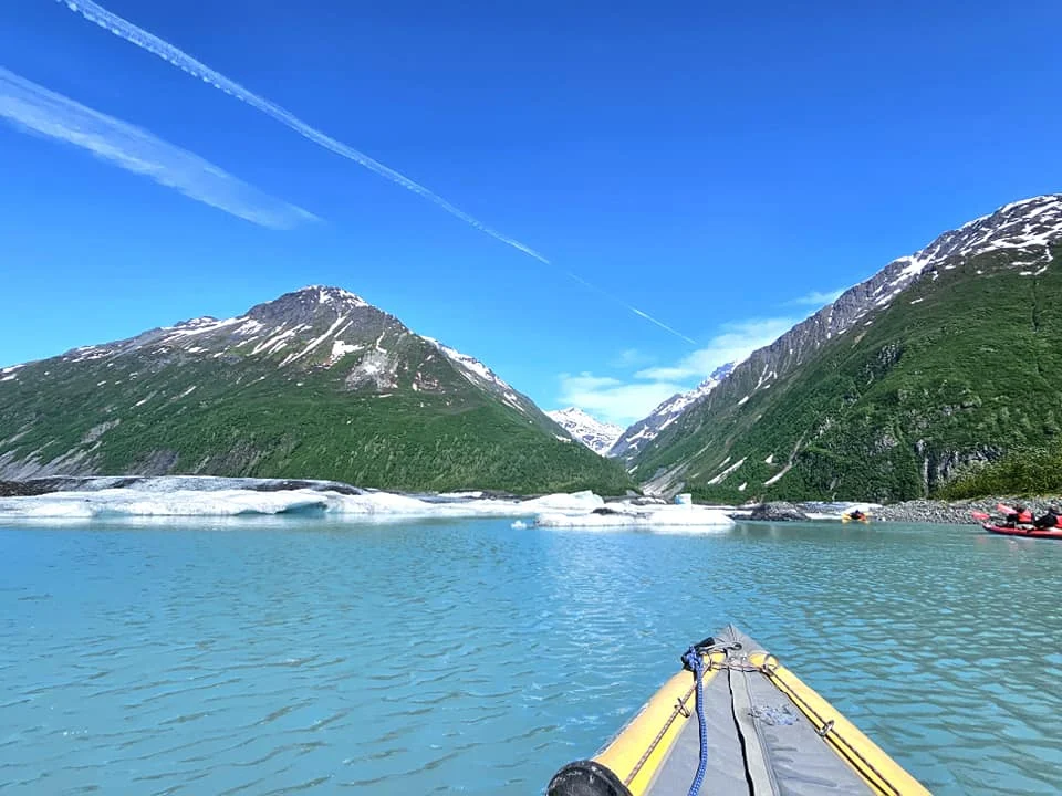 Cruising with Danny and Peter, Holland America Line, Westerdam, Prince William Sound, Valdez, Alaska, United States | A serene panorama of Prince William Sound at dawn, with the luxurious Westerdam cruise ship gliding through calm waters, surrounded by snow-capped mountains and glowing glaciers under a soft pink sky. Humpback whales breach the surface, their tails splashing against the reflective water, while sea otters float playfully in kelp beds and a bald eagle soars overhead. In Valdez Glacier Lake, vibrant blue icebergs drift peacefully, with kayakers in colorful kayaks paddling through the icy maze, dwarfed by the towering Valdez Glacier’s rugged ice face in the background. The Westerdam’s elegant deck features passengers enjoying a gourmet breakfast with panoramic views of the Alaskan wilderness, capturing the harmonious blend of luxury and nature.