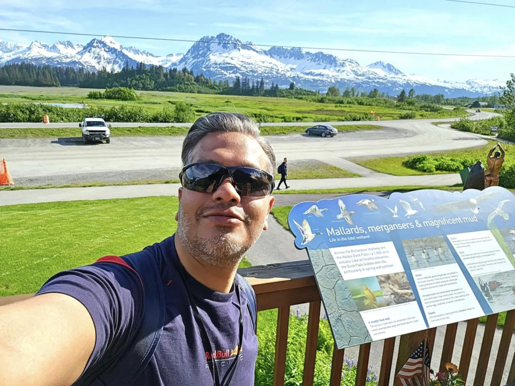 Cruising with Danny and Peter, Holland America Line, Westerdam, Prince William Sound, Valdez, Alaska, United States | A serene panorama of Prince William Sound at dawn, with the luxurious Westerdam cruise ship gliding through calm waters, surrounded by snow-capped mountains and glowing glaciers under a soft pink sky. Humpback whales breach the surface, their tails splashing against the reflective water, while sea otters float playfully in kelp beds and a bald eagle soars overhead. In Valdez Glacier Lake, vibrant blue icebergs drift peacefully, with kayakers in colorful kayaks paddling through the icy maze, dwarfed by the towering Valdez Glacier’s rugged ice face in the background. The Westerdam’s elegant deck features passengers enjoying a gourmet breakfast with panoramic views of the Alaskan wilderness, capturing the harmonious blend of luxury and nature.