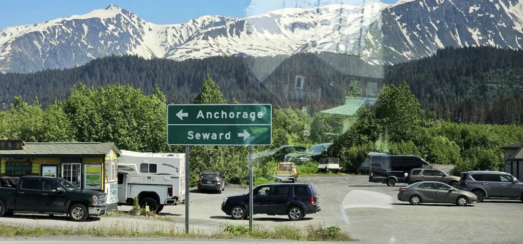 Cruising with Danny and Peter, Holland America Line, Westerdam, Seward, Alaska, United States | A panoramic view of Seward Harbor with rugged cliffs and serene waters, capturing Alaska's wilderness on a photography adventure. Travelers document vibrant wildflowers and snow-capped peaks in Chugach National Forest during an Alaska wilderness cruise. Historical remnants of the 1890 Gold Rush in Seward, including old mining equipment in lush alpine meadows, offer perfect scenes for photography enthusiasts. A majestic bald eagle soars over the tranquil waters of Seward Harbor, while senior-friendly guided tours explore accessible trails amidst stunning natural landscapes.