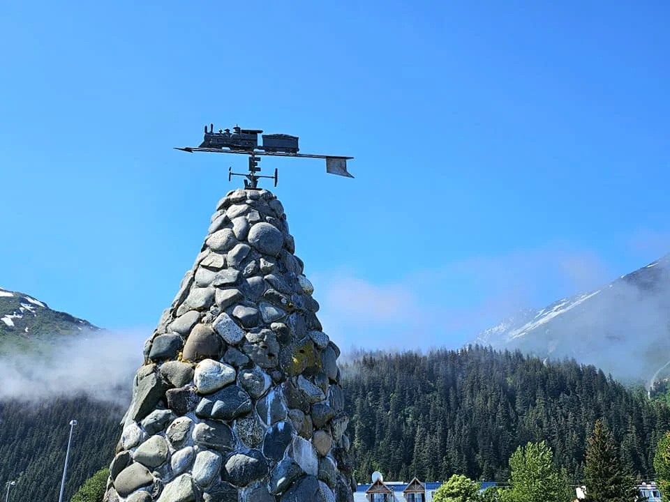 Cruising with Danny and Peter, Holland America Line, Westerdam, Seward, Alaska, United States | A panoramic view of Seward Harbor with rugged cliffs and serene waters, capturing Alaska's wilderness on a photography adventure. Travelers document vibrant wildflowers and snow-capped peaks in Chugach National Forest during an Alaska wilderness cruise. Historical remnants of the 1890 Gold Rush in Seward, including old mining equipment in lush alpine meadows, offer perfect scenes for photography enthusiasts. A majestic bald eagle soars over the tranquil waters of Seward Harbor, while senior-friendly guided tours explore accessible trails amidst stunning natural landscapes.