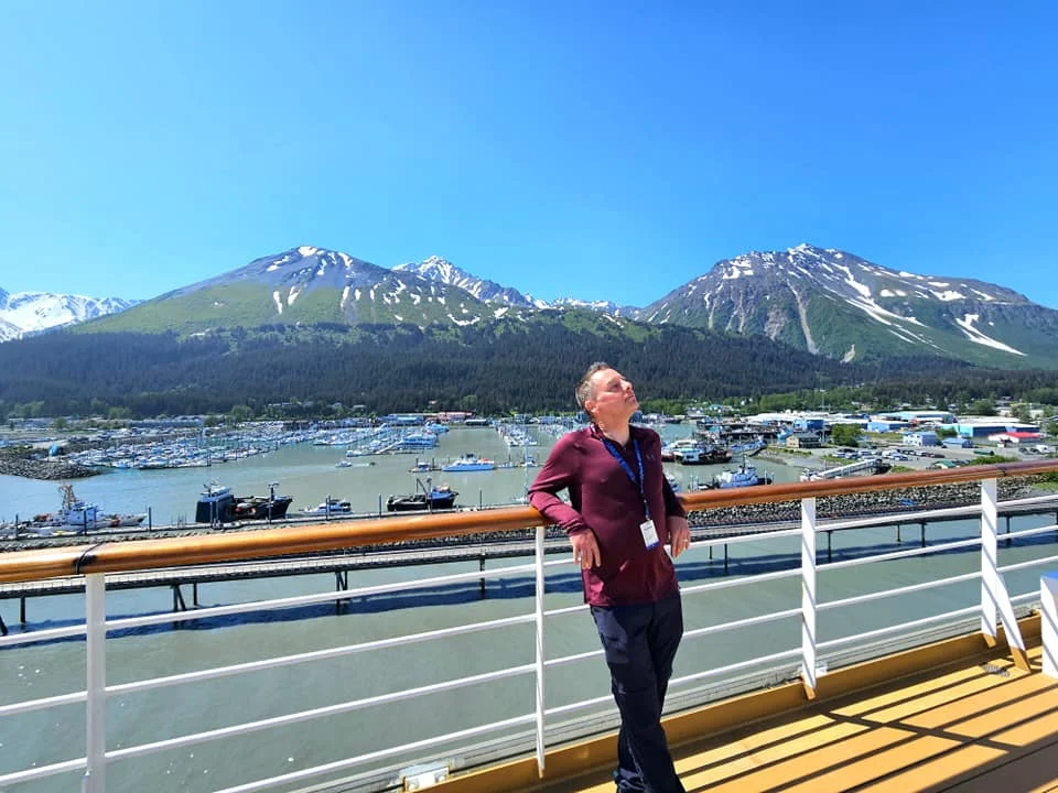 Cruising with Danny and Peter, Holland America Line, Westerdam, Seward, Alaska, United States | A panoramic view of Seward Harbor with rugged cliffs and serene waters, capturing Alaska's wilderness on a photography adventure. Travelers document vibrant wildflowers and snow-capped peaks in Chugach National Forest during an Alaska wilderness cruise. Historical remnants of the 1890 Gold Rush in Seward, including old mining equipment in lush alpine meadows, offer perfect scenes for photography enthusiasts. A majestic bald eagle soars over the tranquil waters of Seward Harbor, while senior-friendly guided tours explore accessible trails amidst stunning natural landscapes.