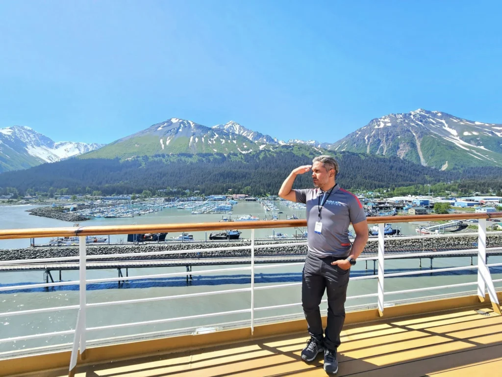 Cruising with Danny and Peter, Holland America Line, Westerdam, Seward, Alaska, United States | A panoramic view of Seward Harbor with rugged cliffs and serene waters, capturing Alaska's wilderness on a photography adventure. Travelers document vibrant wildflowers and snow-capped peaks in Chugach National Forest during an Alaska wilderness cruise. Historical remnants of the 1890 Gold Rush in Seward, including old mining equipment in lush alpine meadows, offer perfect scenes for photography enthusiasts. A majestic bald eagle soars over the tranquil waters of Seward Harbor, while senior-friendly guided tours explore accessible trails amidst stunning natural landscapes.