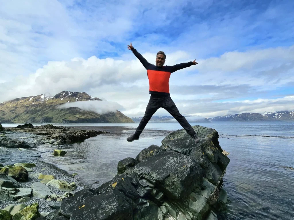 Cruising with Danny and Peter, Holland America Line, Westerdam, Dutch Harbor, Unlaska, Alaska, United States | Scenic view of Dutch Harbor Unalaska featuring rugged mountains and the Bering Sea, with a hiker on Mount Ballyhoo Trail, a majestic bald eagle soaring above, and the historic Russian Orthodox Church with its distinctive onion domes. Includes a fresh seafood dish representing local cuisine and a birdwatching spot at Unalaska Island Bird Sanctuary, capturing the charm of Unalaska's blend of natural beauty, wildlife, and cultural heritage.