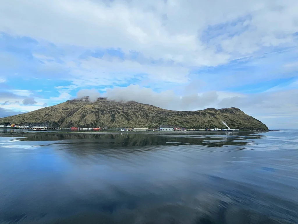 Cruising with Danny and Peter, Holland America Line, Westerdam, Dutch Harbor, Unlaska, Alaska, United States | Scenic view of Dutch Harbor Unalaska featuring rugged mountains and the Bering Sea, with a hiker on Mount Ballyhoo Trail, a majestic bald eagle soaring above, and the historic Russian Orthodox Church with its distinctive onion domes. Includes a fresh seafood dish representing local cuisine and a birdwatching spot at Unalaska Island Bird Sanctuary, capturing the charm of Unalaska's blend of natural beauty, wildlife, and cultural heritage.