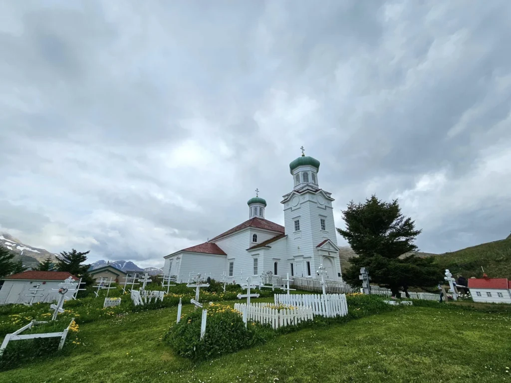 Cruising with Danny and Peter, Holland America Line, Westerdam, Dutch Harbor, Unlaska, Alaska, United States | Scenic view of Dutch Harbor Unalaska featuring rugged mountains and the Bering Sea, with a hiker on Mount Ballyhoo Trail, a majestic bald eagle soaring above, and the historic Russian Orthodox Church with its distinctive onion domes. Includes a fresh seafood dish representing local cuisine and a birdwatching spot at Unalaska Island Bird Sanctuary, capturing the charm of Unalaska's blend of natural beauty, wildlife, and cultural heritage.