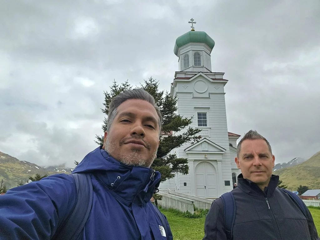 Cruising with Danny and Peter, Holland America Line, Westerdam, Dutch Harbor, Unlaska, Alaska, United States | Scenic view of Dutch Harbor Unalaska featuring rugged mountains and the Bering Sea, with a hiker on Mount Ballyhoo Trail, a majestic bald eagle soaring above, and the historic Russian Orthodox Church with its distinctive onion domes. Includes a fresh seafood dish representing local cuisine and a birdwatching spot at Unalaska Island Bird Sanctuary, capturing the charm of Unalaska's blend of natural beauty, wildlife, and cultural heritage.