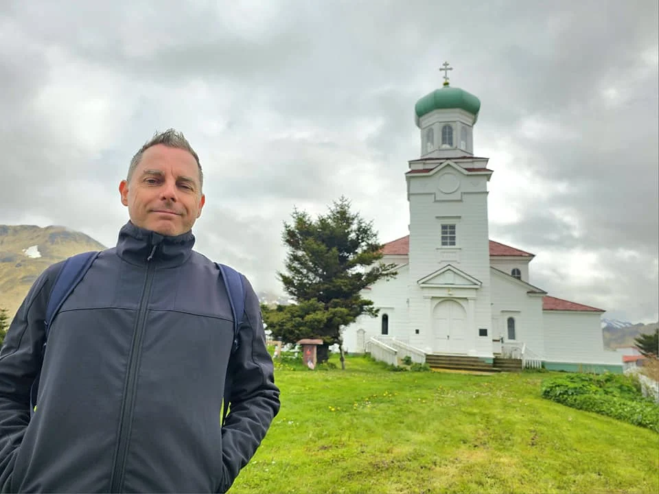 Cruising with Danny and Peter, Holland America Line, Westerdam, Dutch Harbor, Unlaska, Alaska, United States | Scenic view of Dutch Harbor Unalaska featuring rugged mountains and the Bering Sea, with a hiker on Mount Ballyhoo Trail, a majestic bald eagle soaring above, and the historic Russian Orthodox Church with its distinctive onion domes. Includes a fresh seafood dish representing local cuisine and a birdwatching spot at Unalaska Island Bird Sanctuary, capturing the charm of Unalaska's blend of natural beauty, wildlife, and cultural heritage.