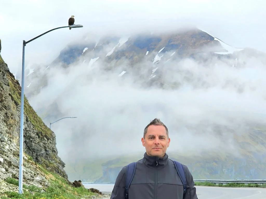 Cruising with Danny and Peter, Holland America Line, Westerdam, Dutch Harbor, Unlaska, Alaska, United States | Scenic view of Dutch Harbor Unalaska featuring rugged mountains and the Bering Sea, with a hiker on Mount Ballyhoo Trail, a majestic bald eagle soaring above, and the historic Russian Orthodox Church with its distinctive onion domes. Includes a fresh seafood dish representing local cuisine and a birdwatching spot at Unalaska Island Bird Sanctuary, capturing the charm of Unalaska's blend of natural beauty, wildlife, and cultural heritage.