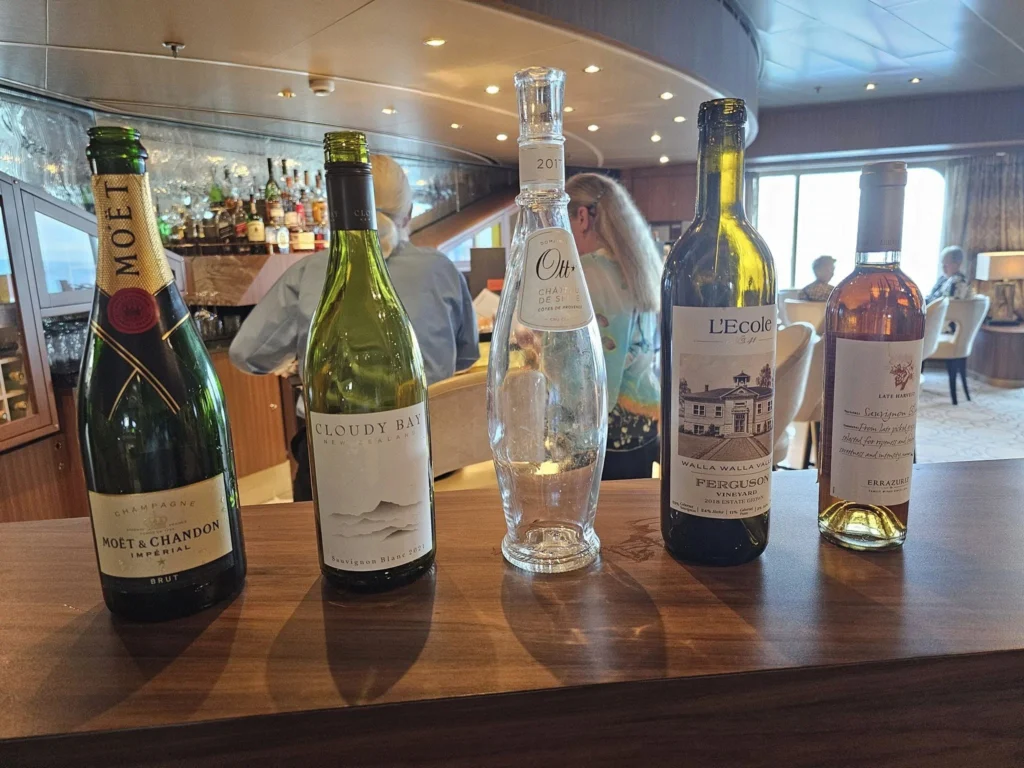 Cruising with Danny and Peter, Holland America Line, Westerdam, Bering Sea, Alaska, United States, Cellar Masters Dinner | A serene view of the Bering Sea from the deck of Holland America Line’s Westerdam during the Alaska Arctic Circle Solstice, with golden sunlight reflecting on calm, shimmering waters under a vast sky. In the distance, a pod of orcas glides gracefully, their black fins cutting through the sea. The ship’s elegant exterior is visible, with passengers wrapped in blankets, gazing at the horizon. Inside, the luxurious Pinnacle Grill dining room glows with soft lighting, showcasing a beautifully set table with crisp white linens, gleaming wine glasses, and a five-course Cellar Master’s Dinner. Plates feature duck confit with roasted cauliflower, porcini soup, warm lobster salad, wagyu beef with mushroom foam, and chocolate pot au crème with Grand Marnier. A sommelier pours Cloudy Bay Sauvignon Blanc, while guests savor the gourmet meal. The scene captures the harmony of Alaska’s wild beauty and refined culinary artistry, with the endless solstice daylight casting a warm, ethereal glow over the sea and ship, blending nature’s grandeur with sophisticated dining.