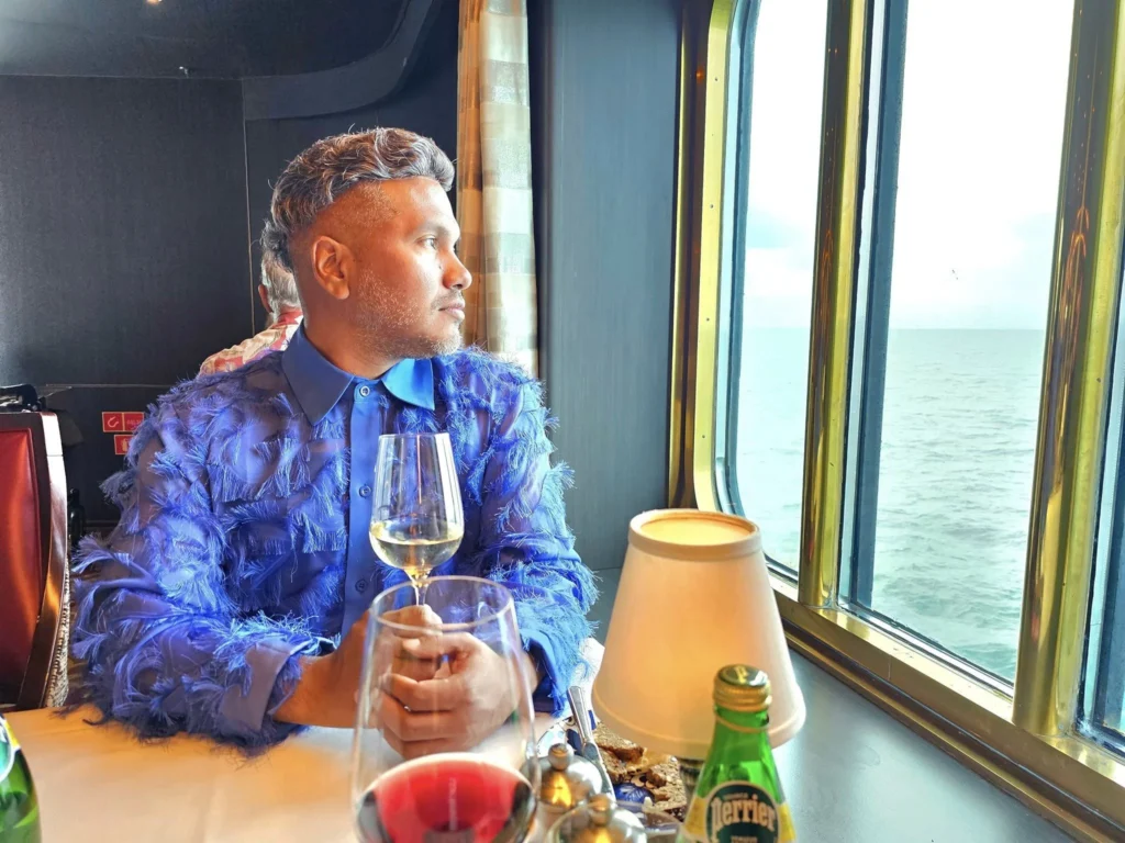 Cruising with Danny and Peter, Holland America Line, Westerdam, Bering Sea, Alaska, United States, Arctic Circle Adventure | A vibrant scene aboard Holland America Line’s Westerdam during the Alaska Arctic Circle Solstice cruise in the Bering Sea, Alaska, United States. Passengers gather around the Lido pool, preparing for the exhilarating Polar Bear Plunge, with crew members setting up the chilled pool to simulate Arctic waters. In the background, stunning Arctic landscapes unfold, featuring pristine ice floes floating on deep blue waters under a golden-hued sky, with distant glaciers and occasional wildlife, such as seals and seabirds, enhancing the untamed beauty of the Frozen Sea Adventure.